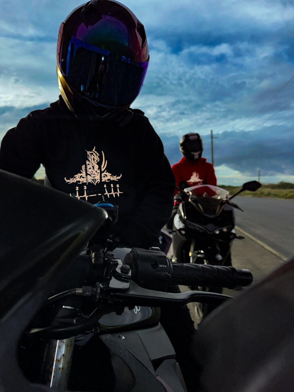two motorcycle riders wearing balaclava hoodies while sitting on motorbikes, showcasing reflective panelling and rider focused design